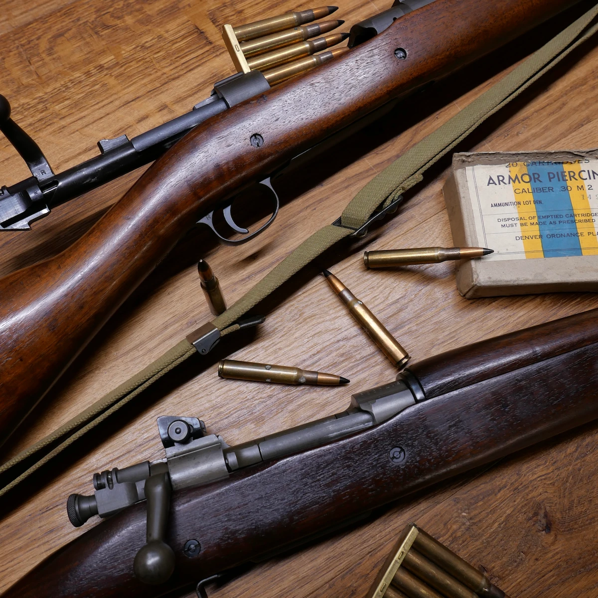 Deux fusils à verrou anciens avec munitions et boîte de cartouches sur table en bois.