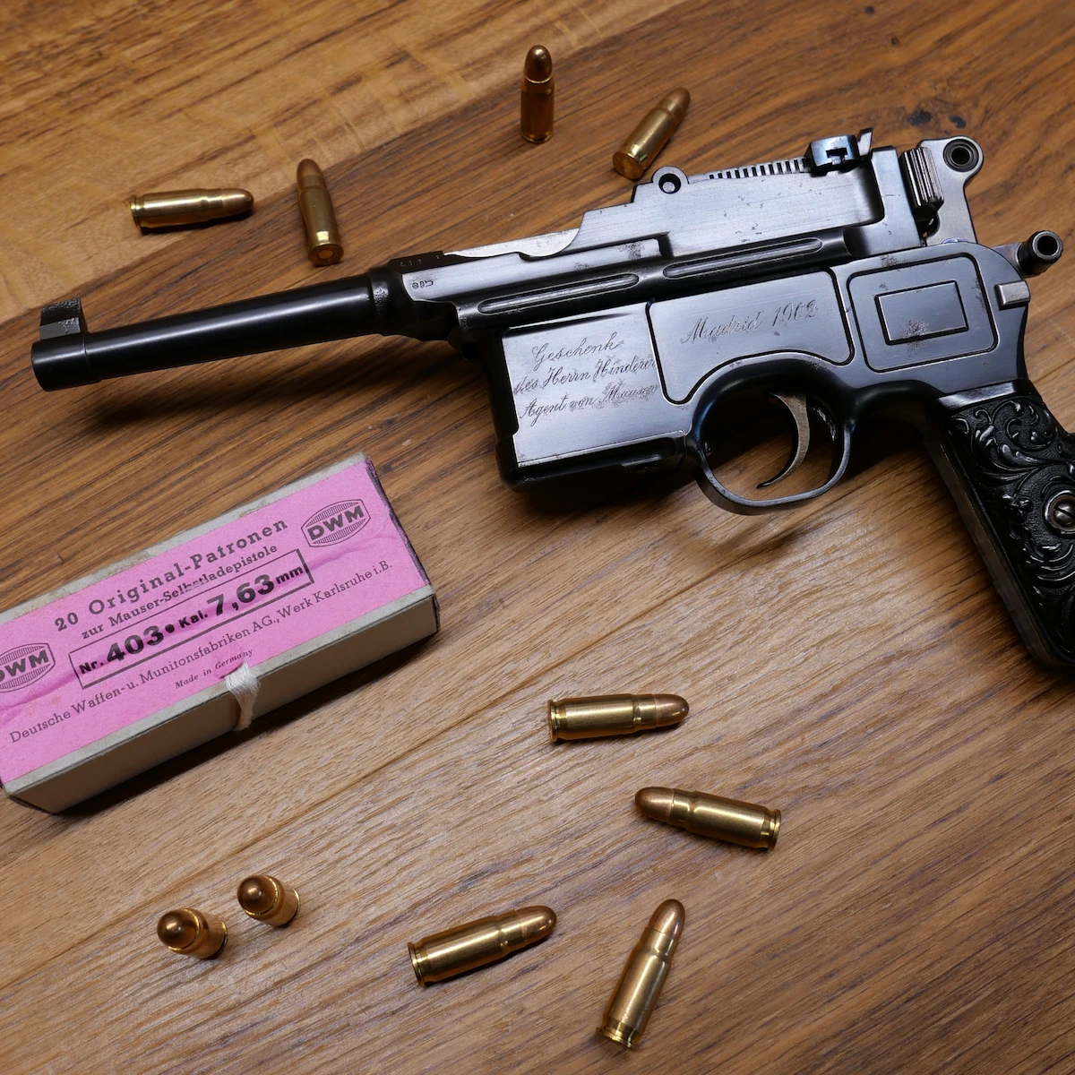 Pistolet Mauser C96 gravé avec munitions et boîte d’origine, sur table en bois.